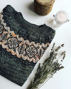 a knitted sweater next to some dried flowers and a candle on a white surface