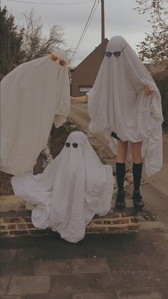 two people dressed in white cloths standing on the side of a road with ghost costumes