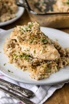 a white plate topped with chicken and rice covered in parsley next to a casserole dish