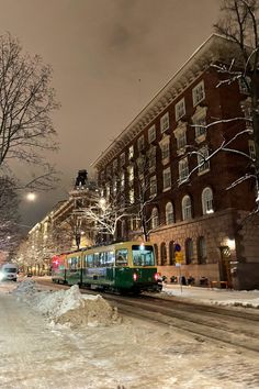 a green bus driving down a snow covered street next to tall buildings at night time