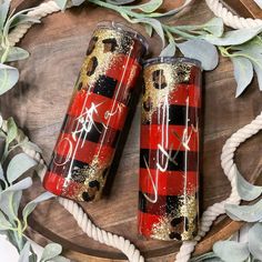 two red and black plaid tumbles sitting on top of a wooden tray with greenery