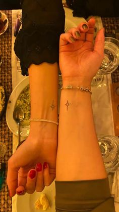 two people holding hands with tattoos on their wrists and one has a cross tattoo