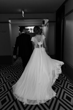 a bride and groom are walking down the hall in black and white, holding hands