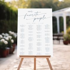 an easel with a seating chart on it in front of some potted plants