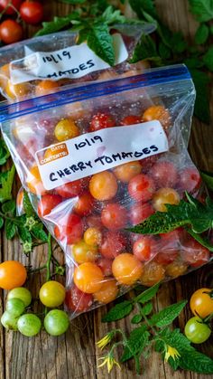 two bags filled with fresh tomatoes sitting on top of a wooden table next to green leaves