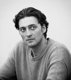 a black and white photo of a man in a sweater looking at the camera with an intense look on his face