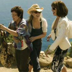 three women standing on top of a hill near the ocean