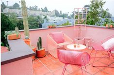 pink chairs and tables on the roof of an apartment building with cactus in the background