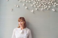 a woman standing in front of a wall with white butterflies on it and looking at the camera