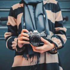 a woman holding a camera in her hands and wearing a scarf around her neck,