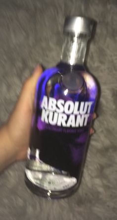 a hand holding a bottle of vodka with the label absolut kurant