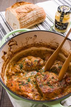 a pot filled with meat and gravy next to sliced bread on a table