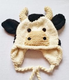 a knitted cow hat with black ears and horns on it's head, sitting on top of a white surface