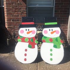 two snowmen standing next to each other in front of a brick wall and door