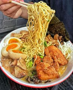 a person holding chopsticks over a bowl of noodles and meat with sauce on the side