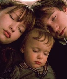 two adults and a child sleeping on top of each other with their heads close together