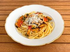 a white plate topped with pasta covered in sauce and toppings on top of a wooden table