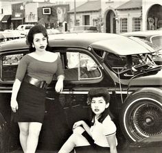 two women are posing in front of an old car