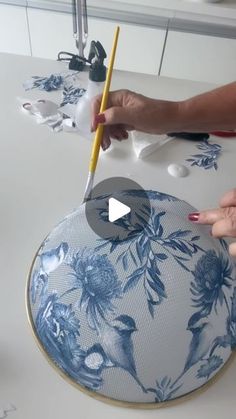 two hands are using a pencil to paint a blue and white floral design on a plate