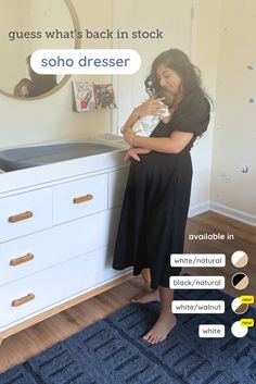 a woman standing in front of a dresser holding a baby