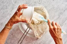 two hands holding a white cup over a marble counter top with an ice cream scooper in it