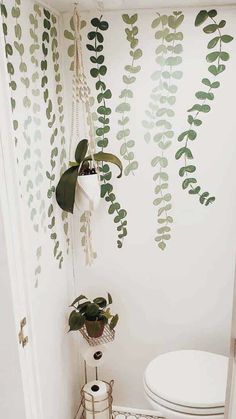 a white toilet sitting in a bathroom next to a wall with plants on the walls