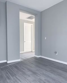 an empty room with gray walls and wood flooring in the foreground is a white door