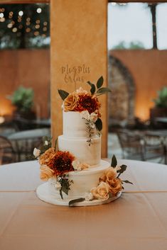 a white wedding cake with orange flowers on the top is sitting on a round table