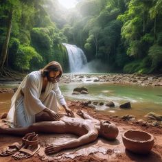 a man is making clay in front of a river and waterfall with his hands on the ground