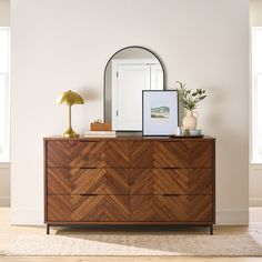 a dresser with a mirror, lamp and pictures on it in a white walled room