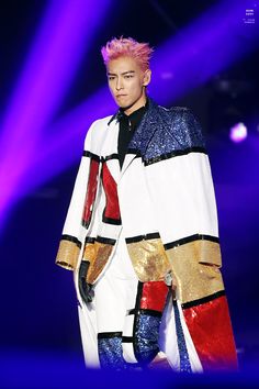 a male in a white jacket and red pants on stage with purple lights behind him