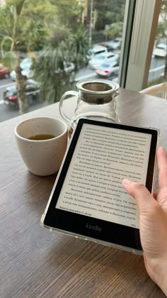 a person is holding an electronic device at a table with a cup of coffee and a window