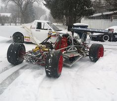 an off - road race car is parked in the snow next to a white truck