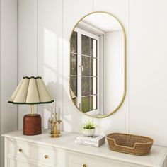 a white dresser topped with a mirror next to a lamp and a basket on top of it