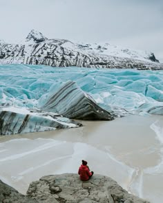 a man sitting on top of a rock next to a body of water and ice