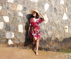 a woman standing next to a stone wall wearing a hat and holding her hand on her head