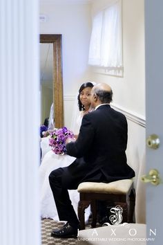 a man and woman sitting on a bench in front of a mirror with purple flowers