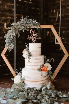 a white wedding cake with greenery and an acrylic sign that says our adventure