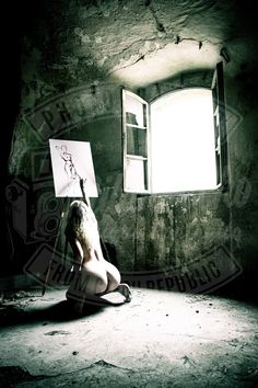 a naked woman sitting on the ground holding a drawing board in front of an open window