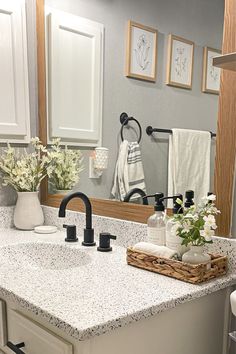 a bathroom with white cabinets and marble counter tops, black faucet, and flowers on the sink