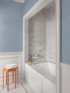 a bathroom with blue walls and white tile on the wall, two stools in front of the bathtub