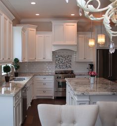 a kitchen with white cabinets and marble counter tops