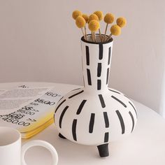 a white vase with yellow flowers in it on a table next to a coffee cup