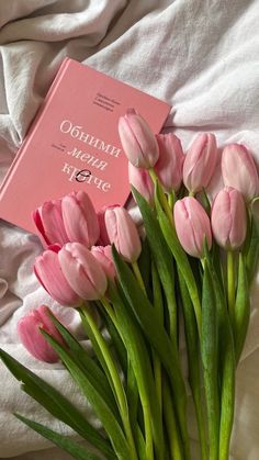 pink tulips are arranged in front of a book on a white bed sheet