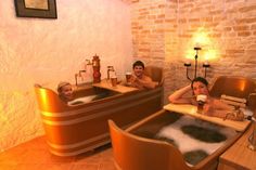 two people sitting in bathtubs with soap on the floor and one person holding a cup