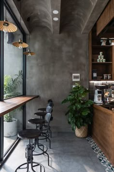 a bar with stools and potted plants in front of the counter, next to a large window