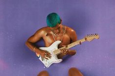 a man with blue hair playing an electric guitar on a purple background in front of his legs