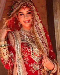 a woman in a red and gold bridal outfit posing for the camera with her hands on her hips