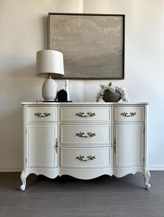 a white dresser sitting next to a painting on the wall