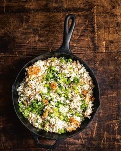 a skillet filled with rice and vegetables on top of a wooden table